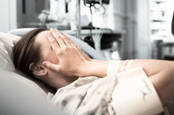 Woman in hospital (in hospital gown) covers face with hands 