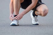 Man ties laces on running shoe pre-jog. Photo by Shutterstock
